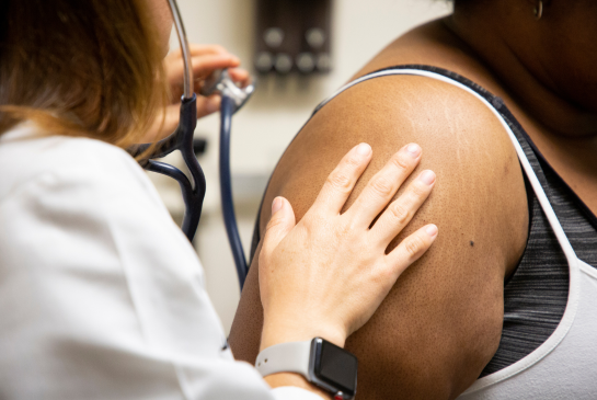 Doctor touches patient's shoulder while using a stethoscope on patient.